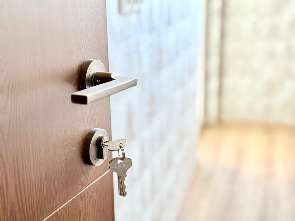 A close-up of a wooden door with a modern metal handle and a key in the lock, slightly ajar.