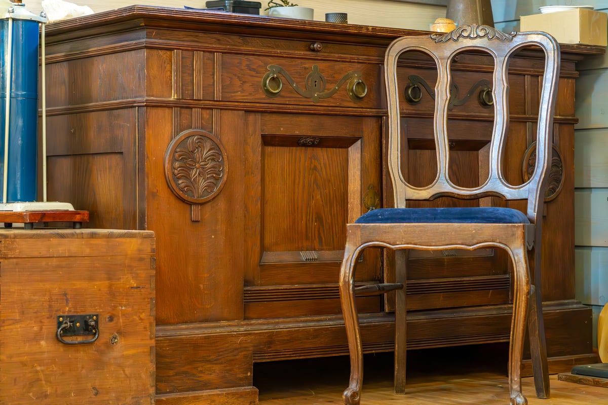 vintage wooden sideboard with carved details and brass handles, accompanied by an elegant wooden chair featuring a blue upholstered seat.