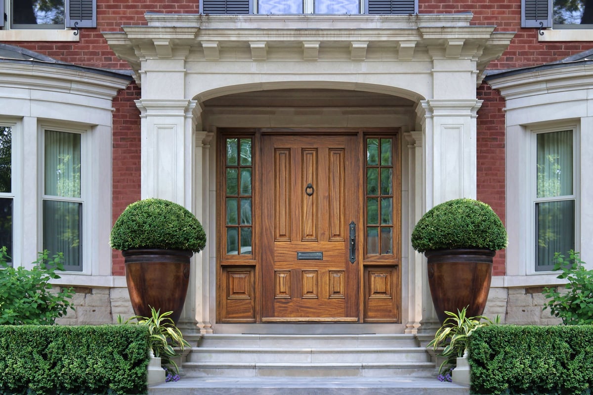 Elegant portico entrance of home with wood grain front door and bay windows