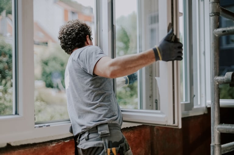 One young handsome Caucasian man in a gray uniform stands from the back and repairs installing a window frame in a house